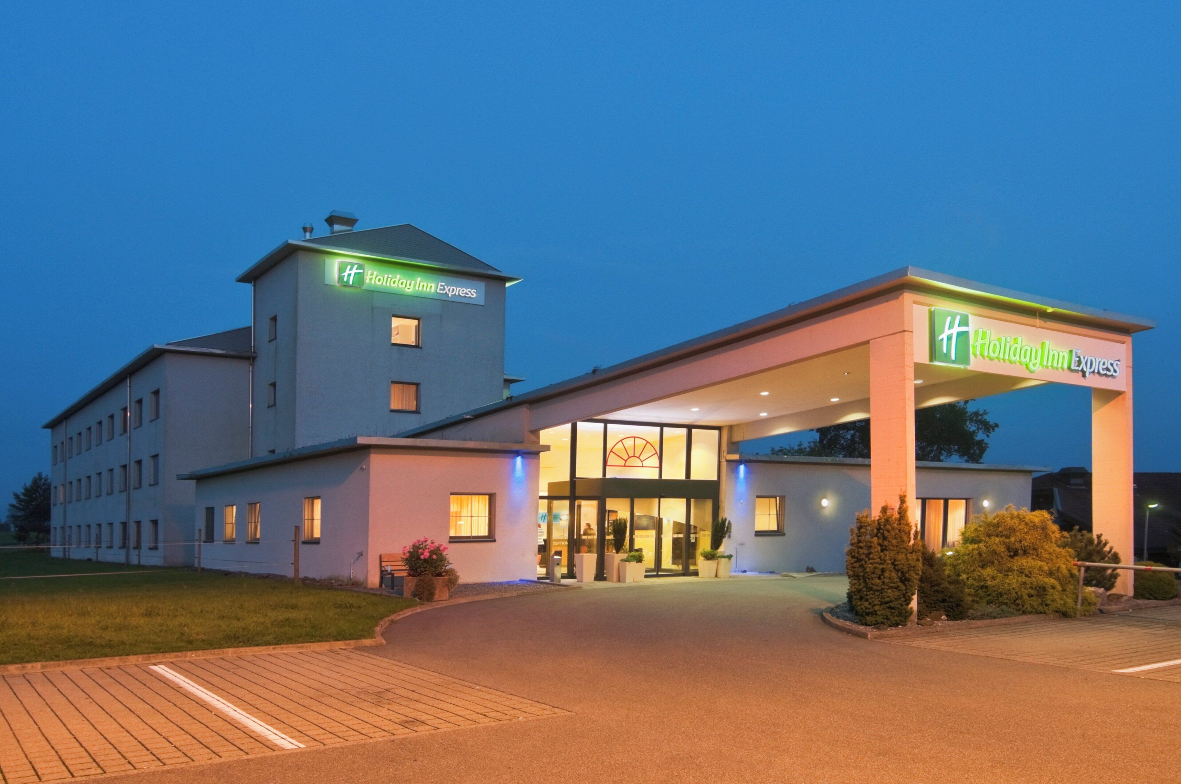 Ein Holiday Inn Express Hotel mit modernem Design, das eine markante Eingangspartie und einen Parkplatz bietet.