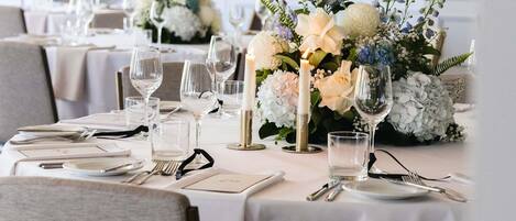 Ein Esstisch, festlich gedeckt für eine formelle Veranstaltung, mit weißen Tischdecken, Gläsern und floralen Tischdekorationen.