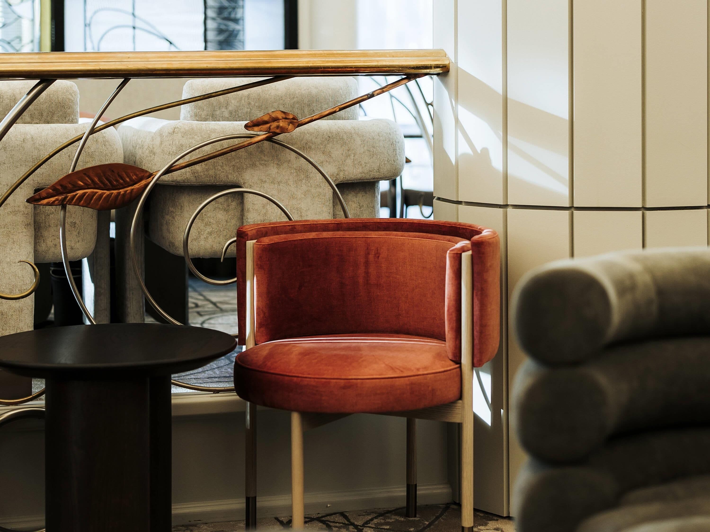 Un intérieur moderne avec un fauteuil en velours rouge, une petite table ronde et une structure métallique originale ornée de motifs de feuilles.