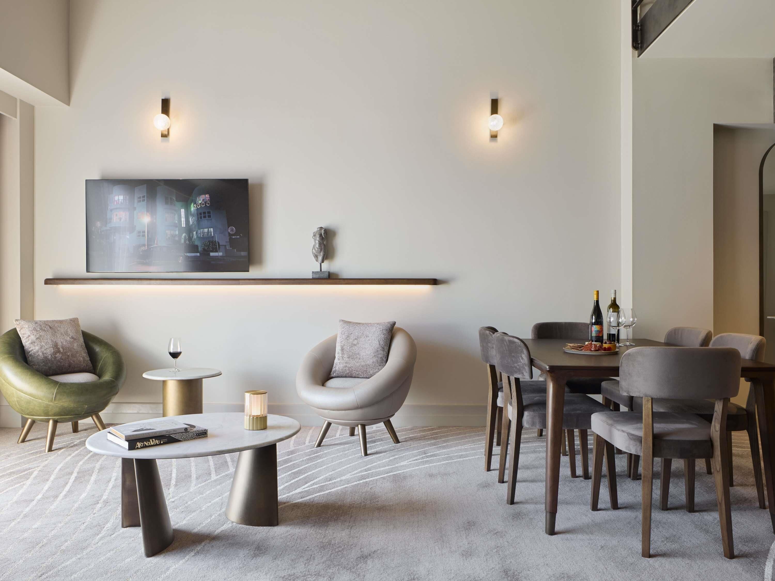 A modern dining area with a round table, two chairs, a small side table, and a decorative wall piece.