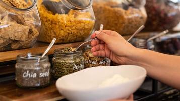 Iemand selecteert granola uit een pot met de aanduiding 'Chia zaad' en 'Pepitas'.