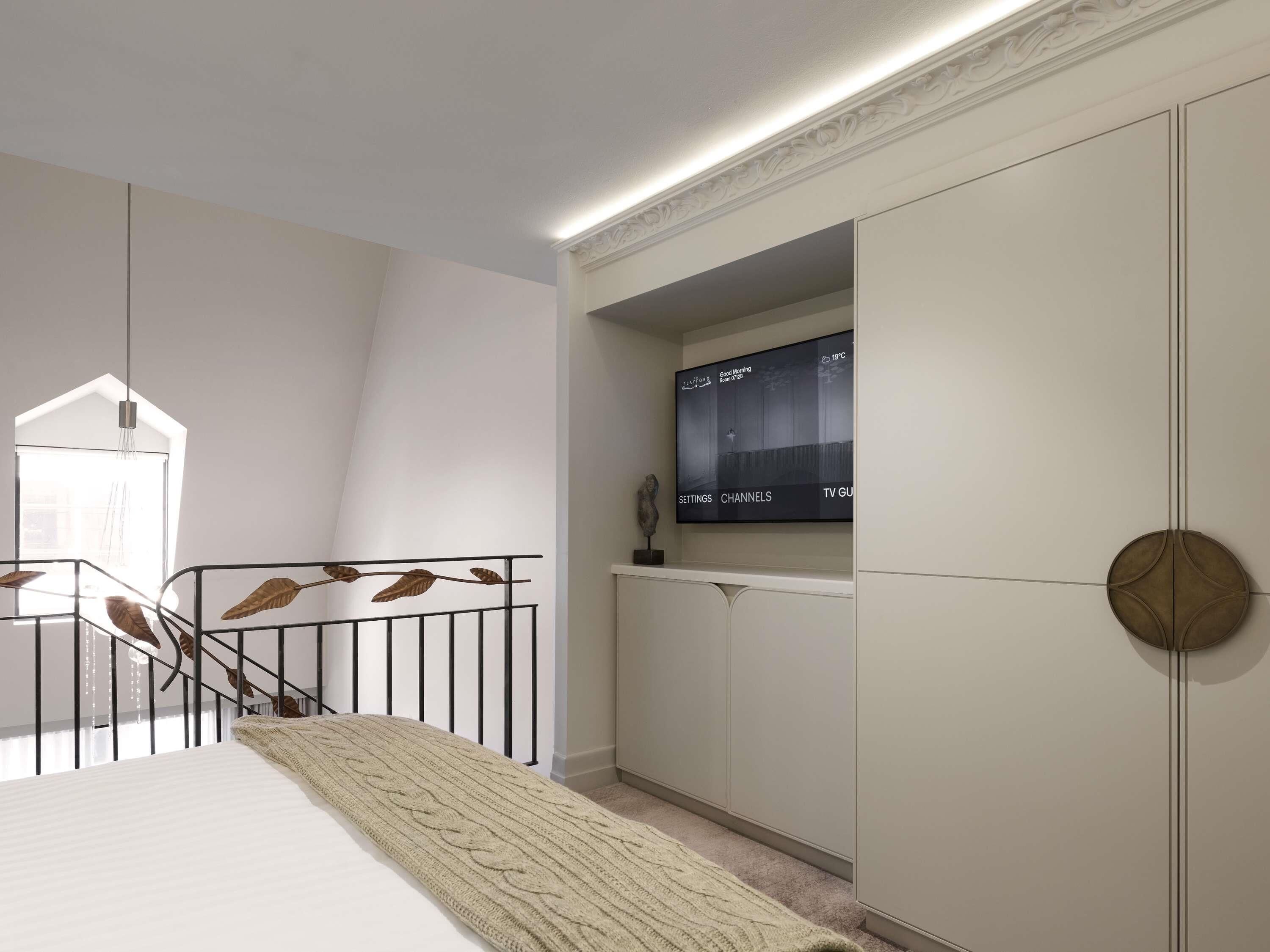Un dormitorio con una cama, un televisor instalado en la pared y una escalera con barandilla.