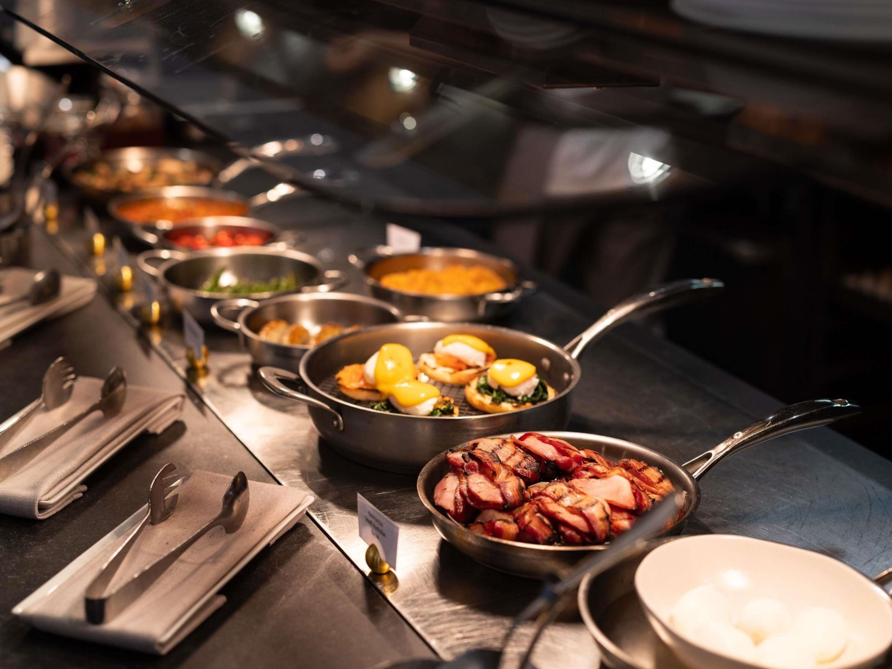 Una barra de buffet con diversos platos, incluyendo mariscos y carne, además de cubiertos para los comensales.
