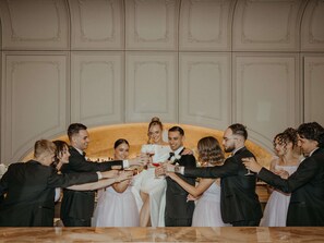 A group of people toasting with champagne glasses in a room with a marble table and ornate wall paneling.