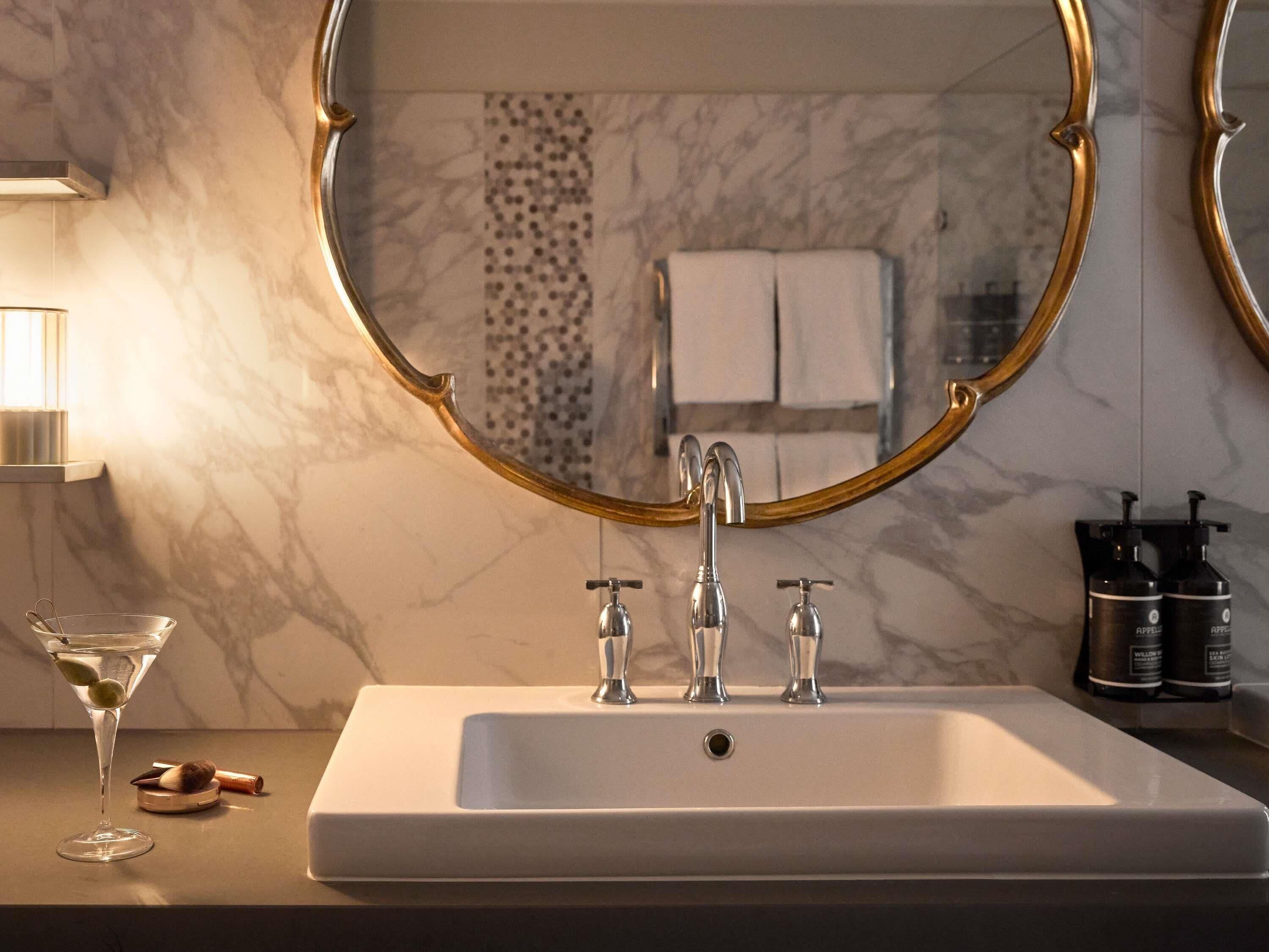Un baño con lavamanos de mármol, espejo con marco dorado y artículos de aseo.