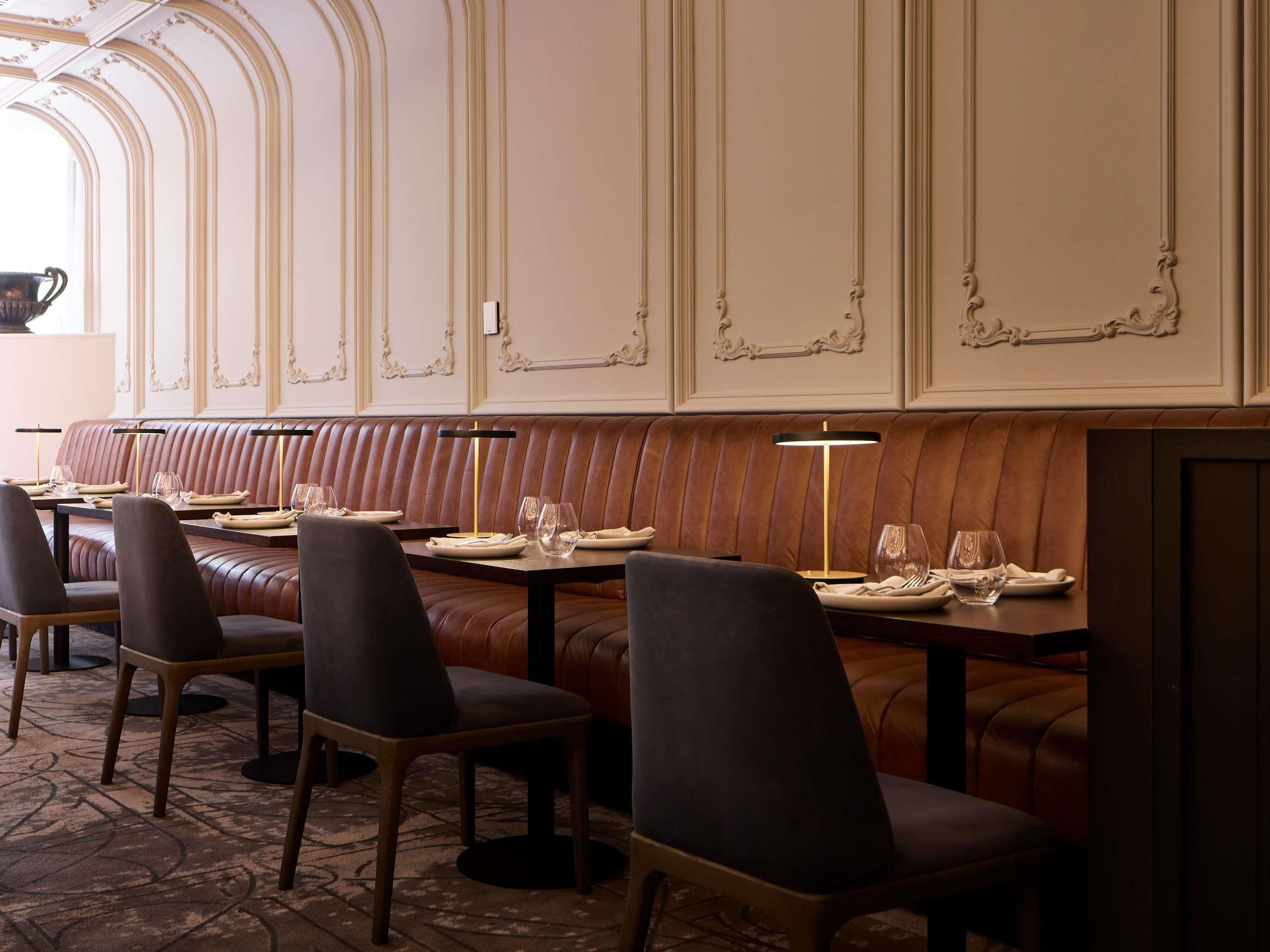 En restaurang med läderbeklädda bås och bord, där varje bord är dukat med tallrikar och glas.