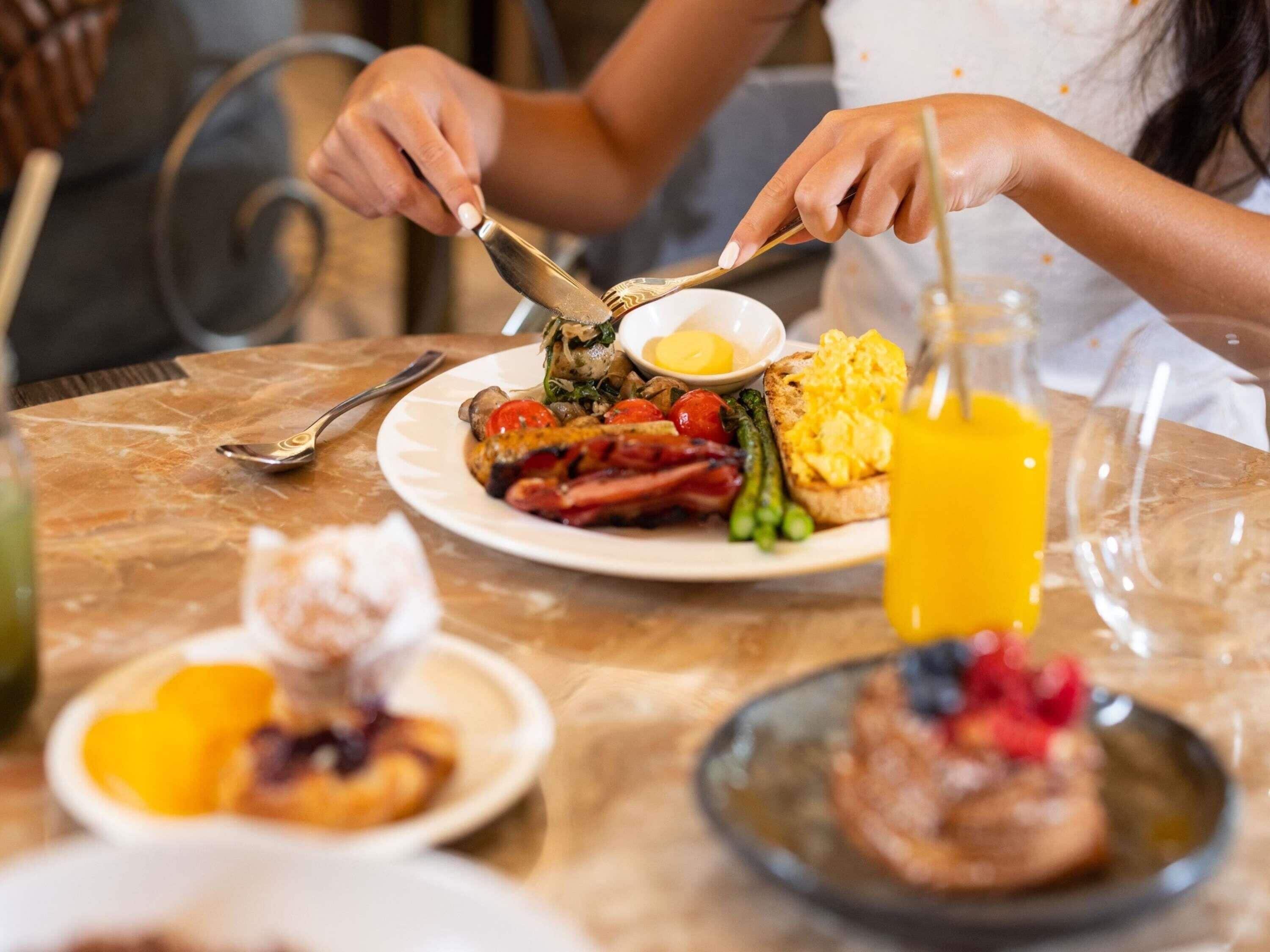 Desayuno con un plato de comida, un vaso de jugo de naranja y un tenedor y cuchillo sobre una mesa de mármol.