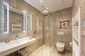 A modern bathroom with a glass-enclosed shower, a white sink, and a toilet.