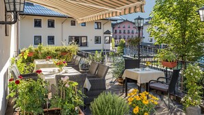 Eine Terrasse im Freien mit Korbmöbeln, Blumentöpfen und Esstischen.