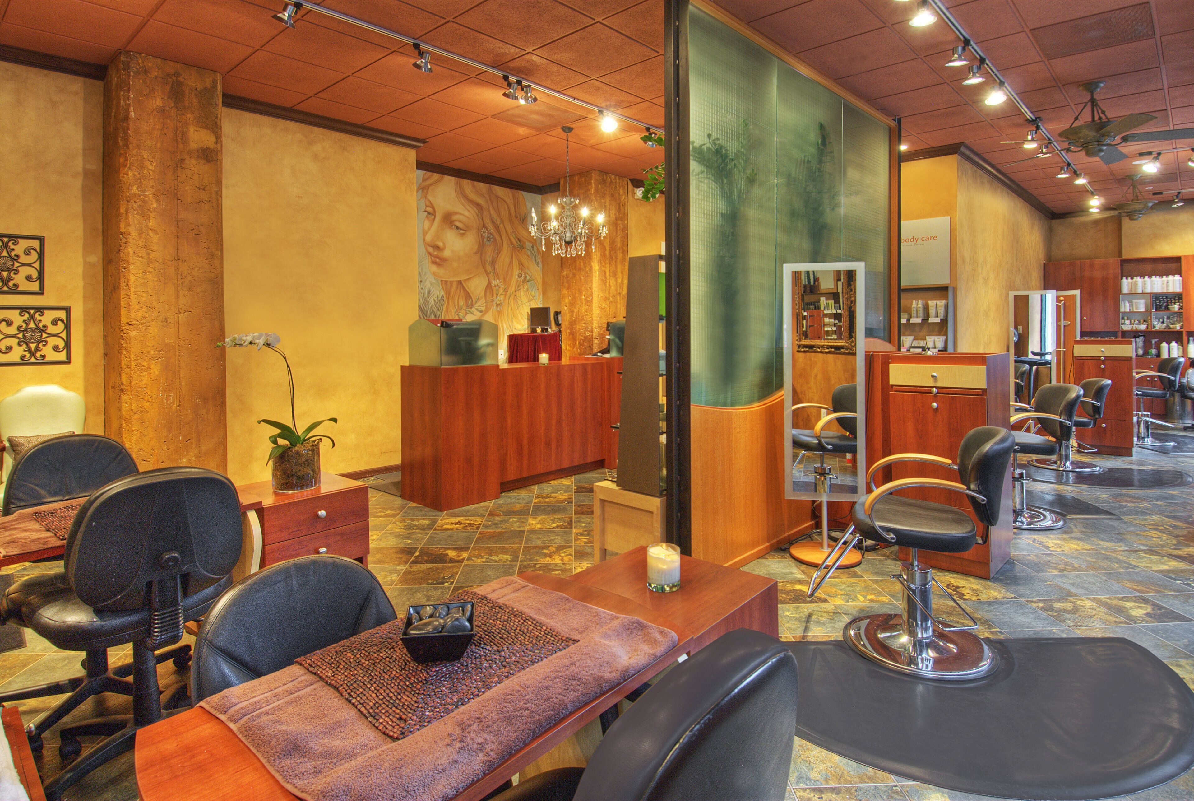A hair salon interior with multiple seating areas, a reception desk, and a mirror reflecting the salon's interior.