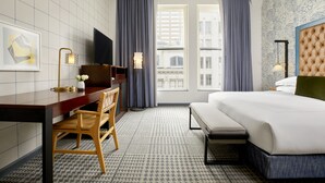 A hotel room with a bed, a desk, a chair, a TV, and a window with curtains.