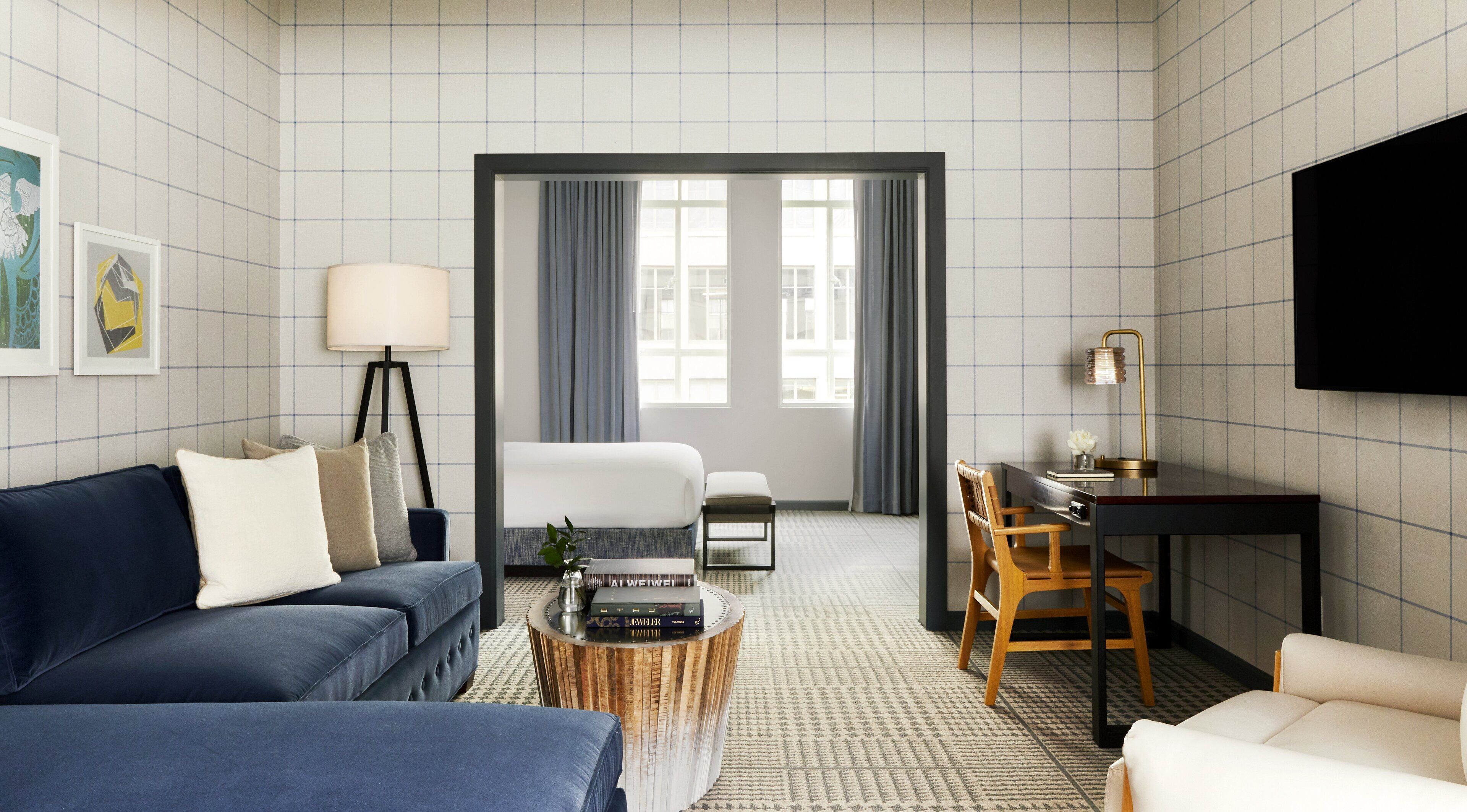 A hotel room with a blue sofa, a bed, a desk, and a television.