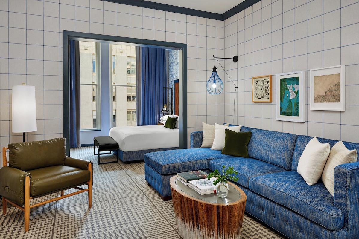 A hotel room with a bed, a sofa, a chair, a coffee table, and artwork on the walls.