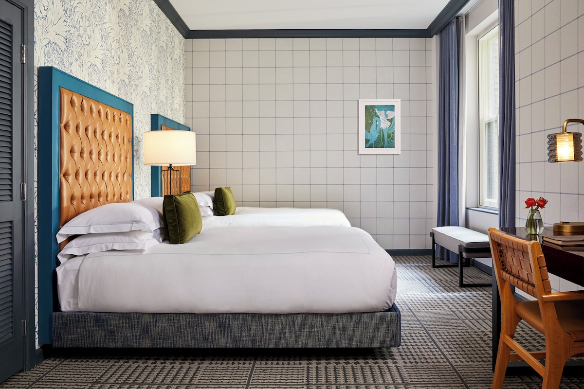 A hotel room with a large bed, a desk with a chair, a lamp, and a window with curtains.