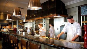 A commercial kitchen with chefs preparing food, stainless steel appliances, and a menu board.