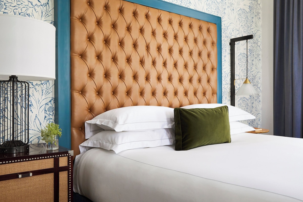 A hotel room with a tufted headboard, white bedding, and a green pillow.