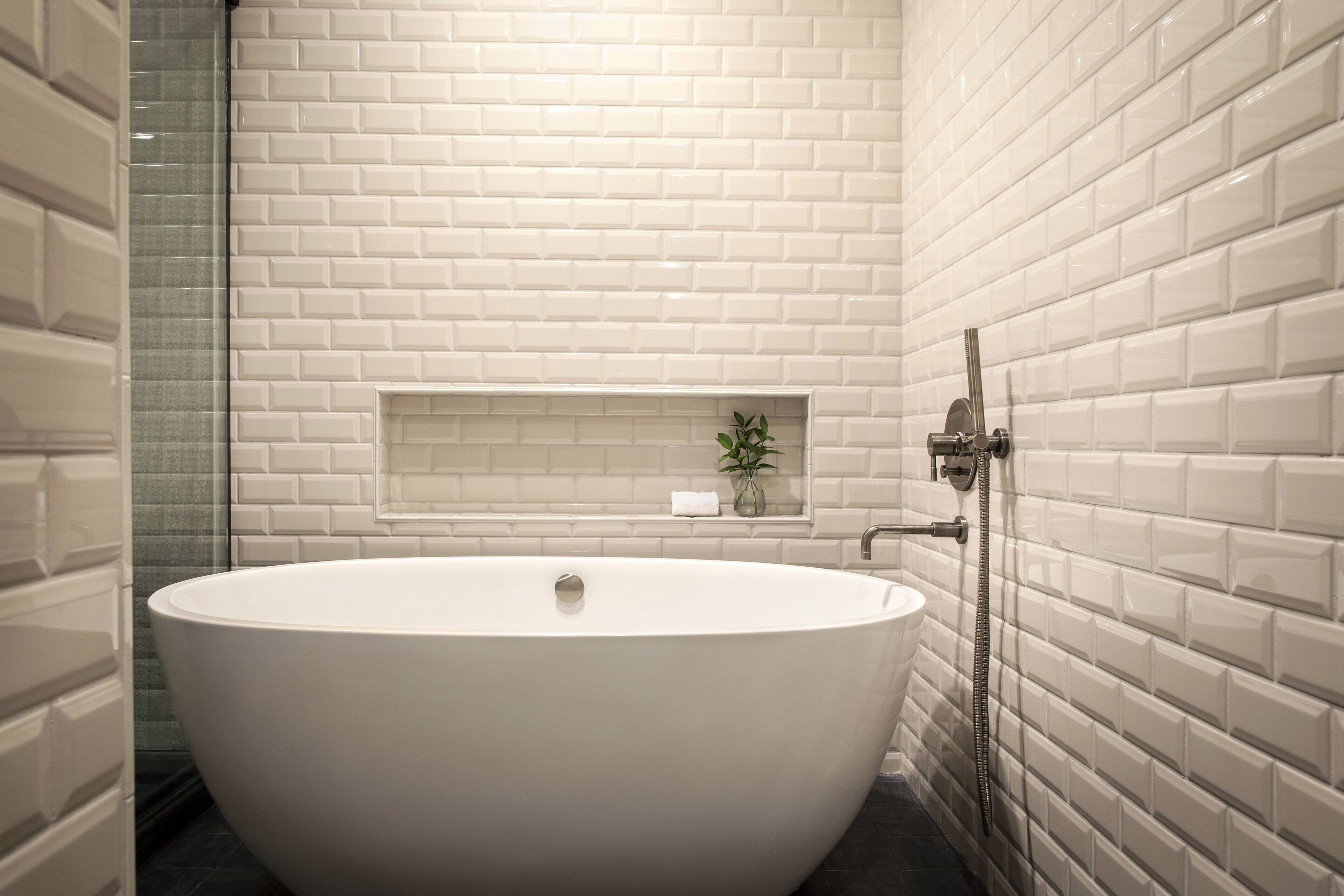 A modern bathroom with a freestanding bathtub, a glass shower enclosure, and a small shelf with a plant.