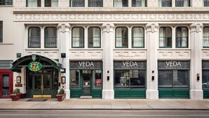 Ein Gebäude mit drei Eingängen zum VEDA Salon und Spa, jeweils mit einer grünen Tür und großen Fenstern.