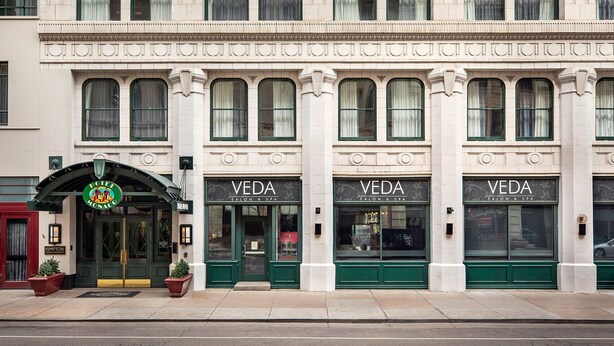 A building with three VEDA salon and spa entrances, each with a green door and large windows.