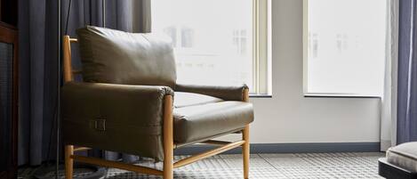 A modern armchair with a wooden frame and leather upholstery, positioned in a room with patterned carpet and large windows.