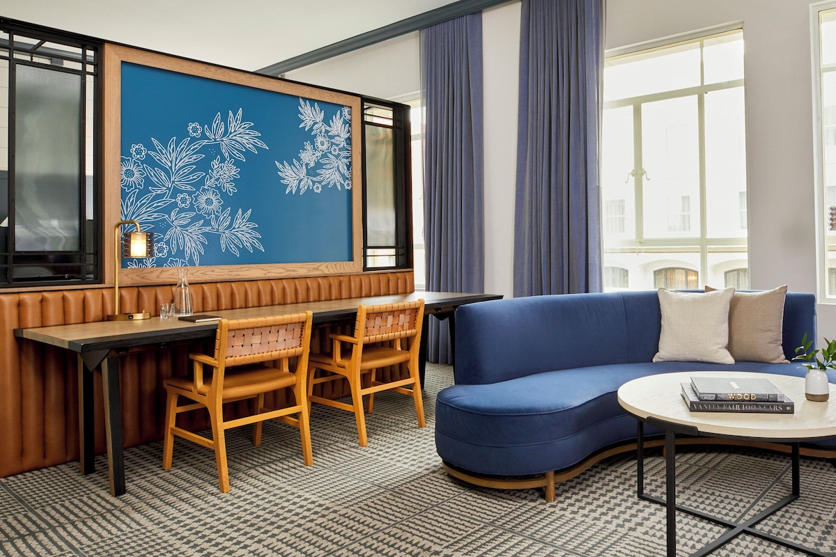 A hotel room with a seating area, a sofa, a round table, and a decorative wall with floral patterns.