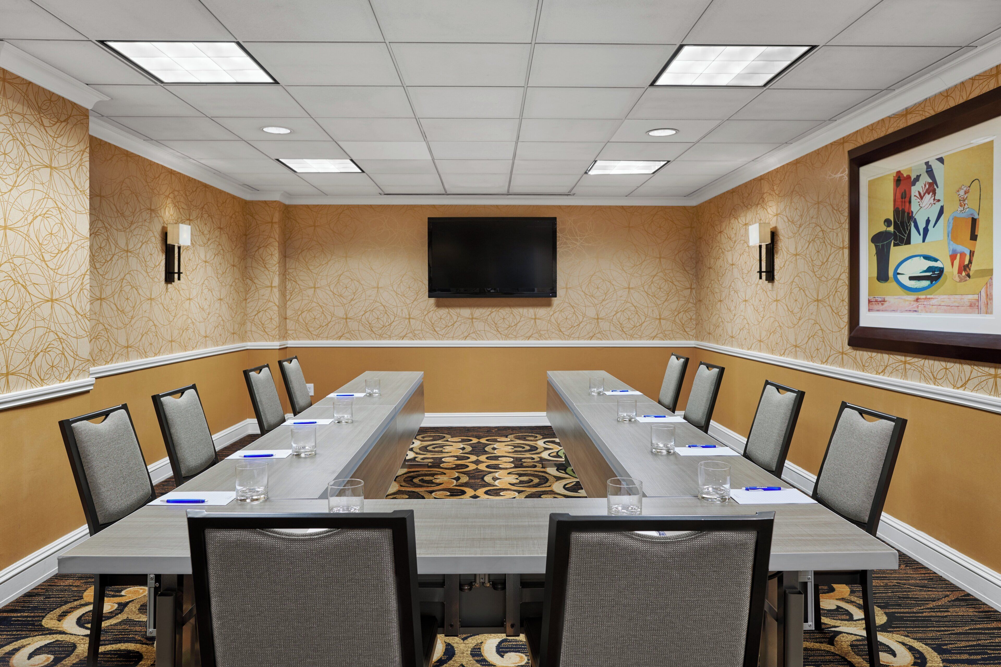 A conference room with a long table, chairs, a flat-screen TV, and patterned carpet.