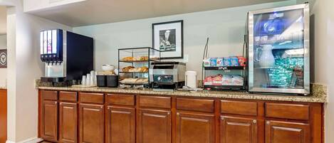 A hotel kitchen with a self-serve coffee station, a refrigerated display case, and a variety of baked goods.