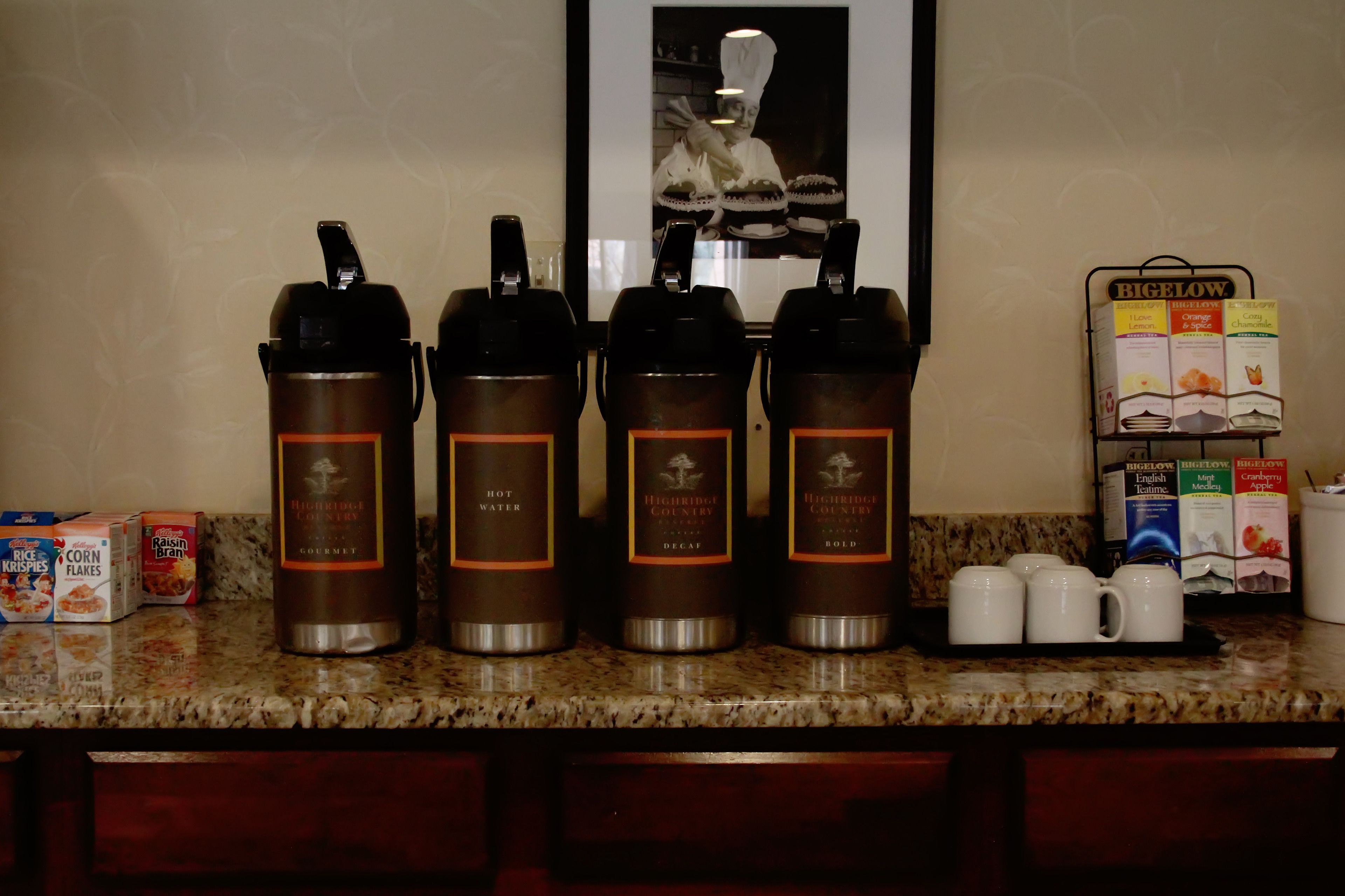A kitchen counter with four hot water dispensers, a coffee machine, and a rack of coffee pods.