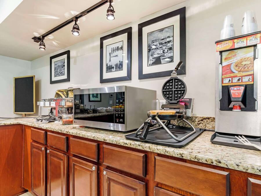 A kitchen with a microwave, coffee machine, and a waffle maker. There are framed pictures on the wall and a speaker on the left.