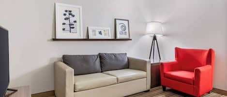 A room with a beige sofa, a red armchair, a floor lamp, and framed artwork on the wall.