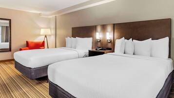 A hotel room with two queen beds, a red chair, a nightstand with a phone, and a wall-mounted lamp.