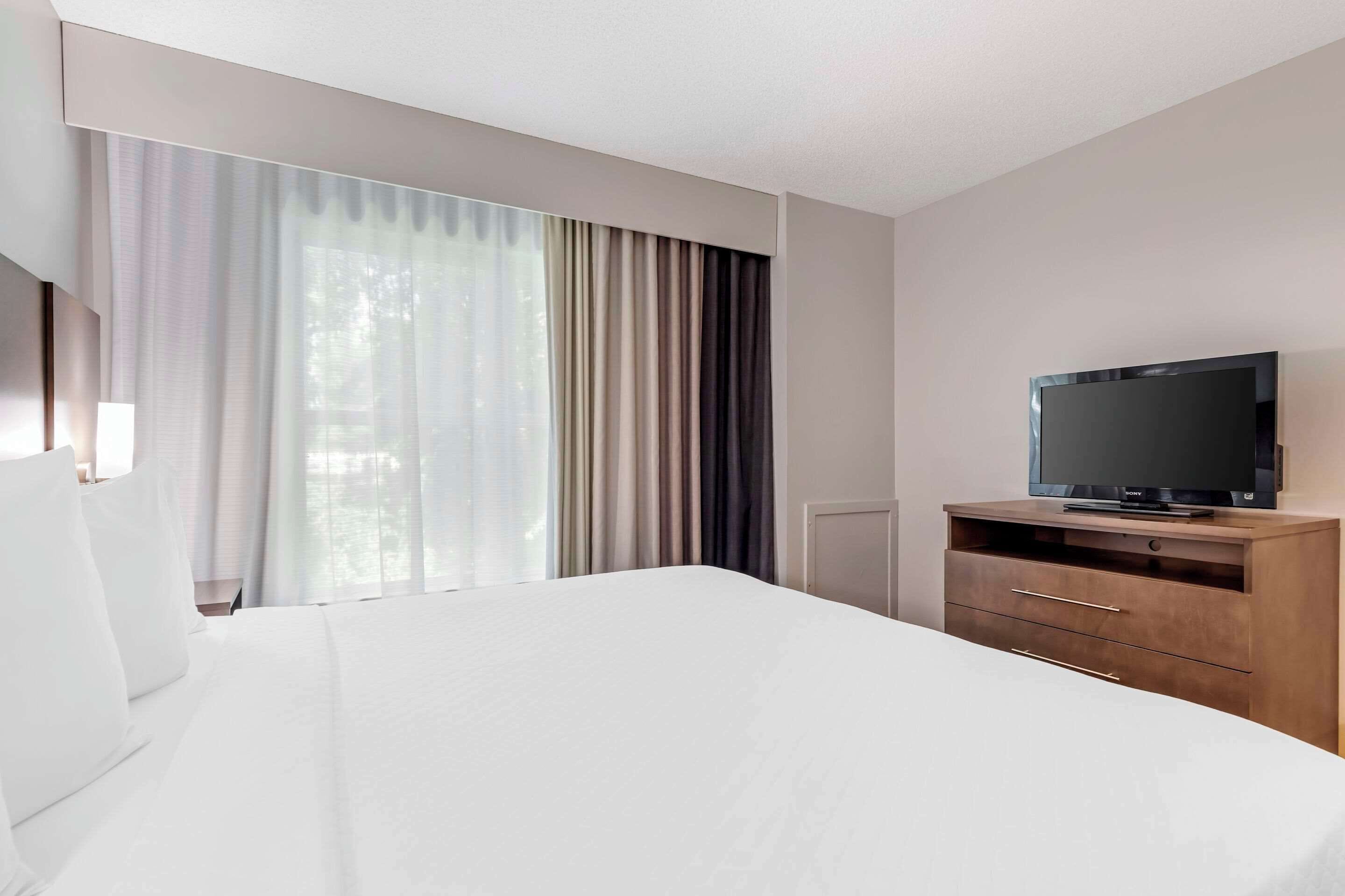 A hotel room with a large bed, a TV on a wooden cabinet, and a window with curtains.