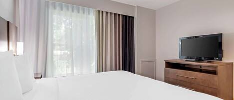 Habitación de hotel con una cama grande, un televisor sobre un mueble de madera y una ventana con cortinas.