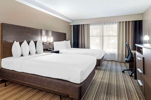 A hotel room with two beds, a desk, a chair, and a large window with curtains.