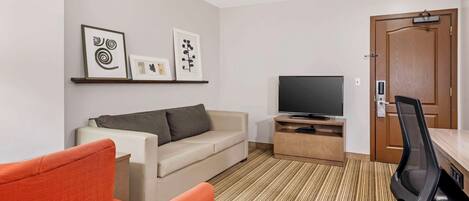 A modern hotel room with a beige sofa, a red armchair, a flat-screen TV, a wooden side table, and a door with a handle.