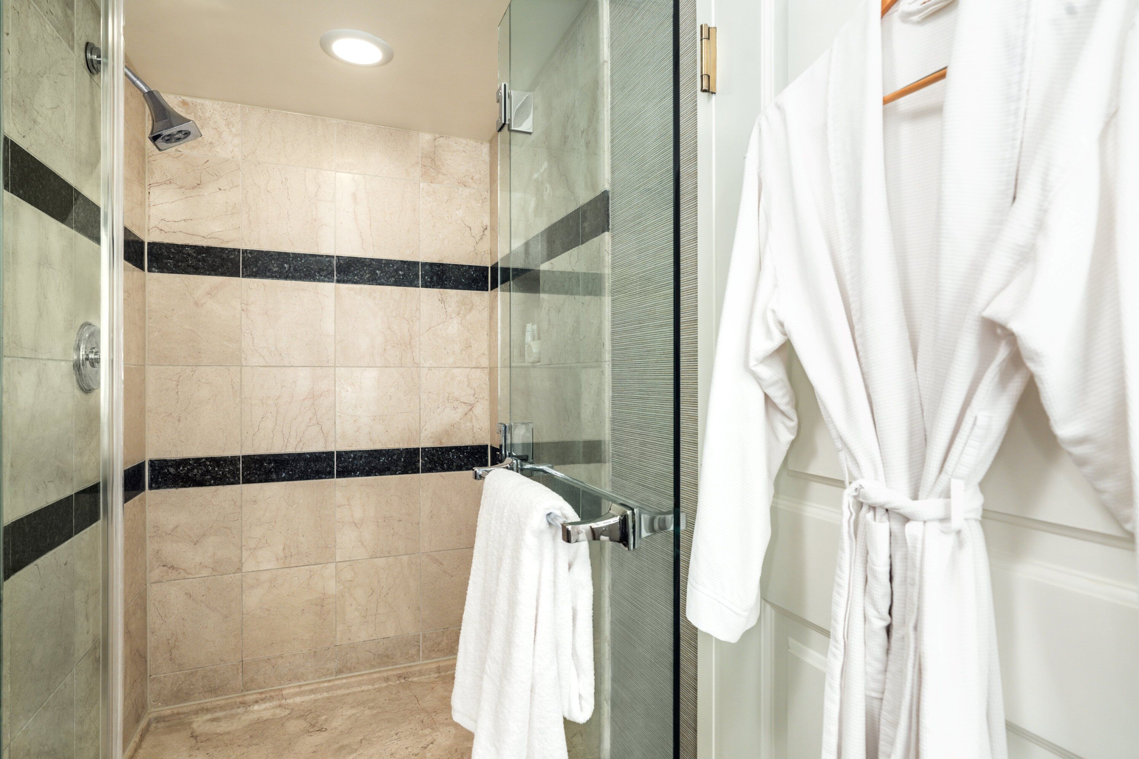 Un baño moderno con cabina de ducha de vidrio, un perchero y una bata colgada en la puerta.