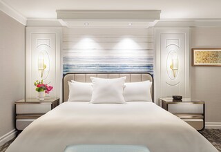 A hotel room with a large bed, two bedside tables, a nightstand, a wall-mounted lamp, and a framed picture.