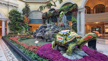 A grand atrium with a decorative fountain, lush greenery, and a large, colorful sculpture of a mythical creature.