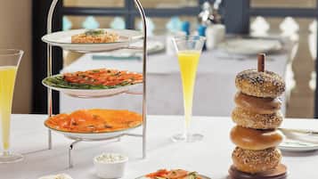 A three-tiered dessert stand with various dishes, a stack of bagels, and a glass of orange juice on a table.