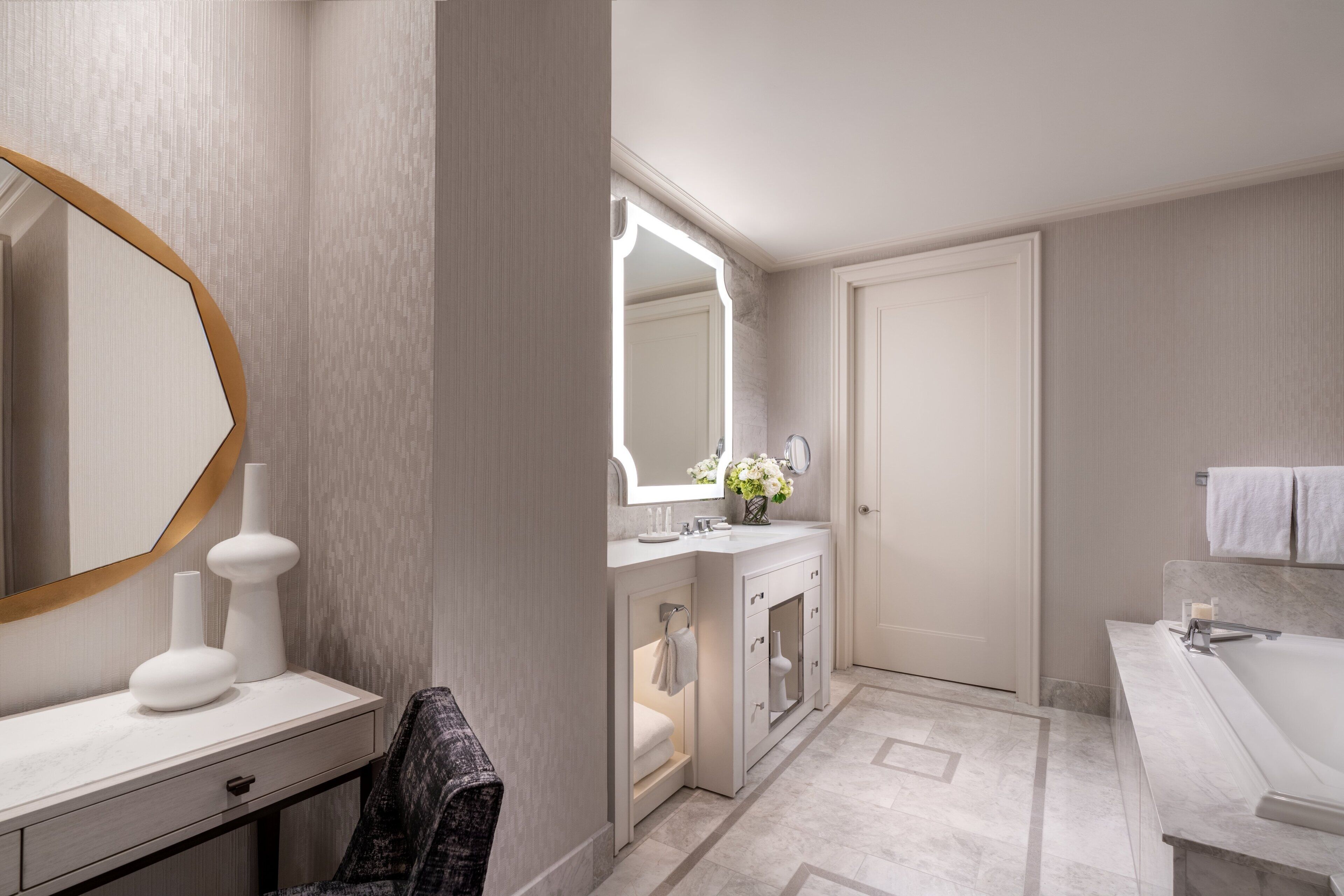 A modern bathroom with a large mirror, a vanity with a sink, a bathtub, and a door leading to another room.