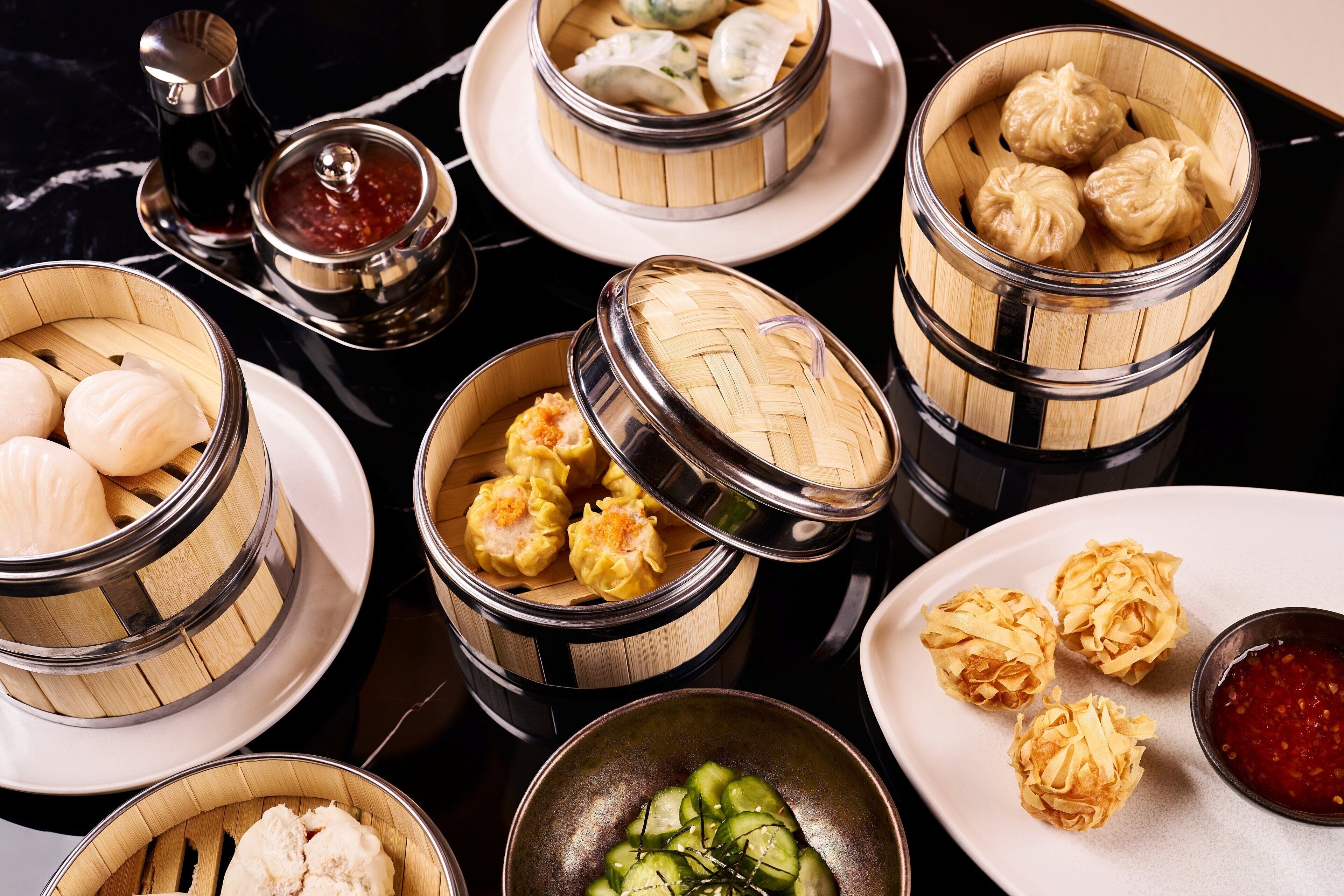A variety of dim sum dishes in bamboo steamers, including dumplings and buns, served on plates with dipping sauces.