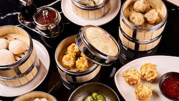 Diverse dim sum gerechten in bamboestoompjes, waaronder dumplings en broodjes, gepresenteerd op borden met dipsaus.