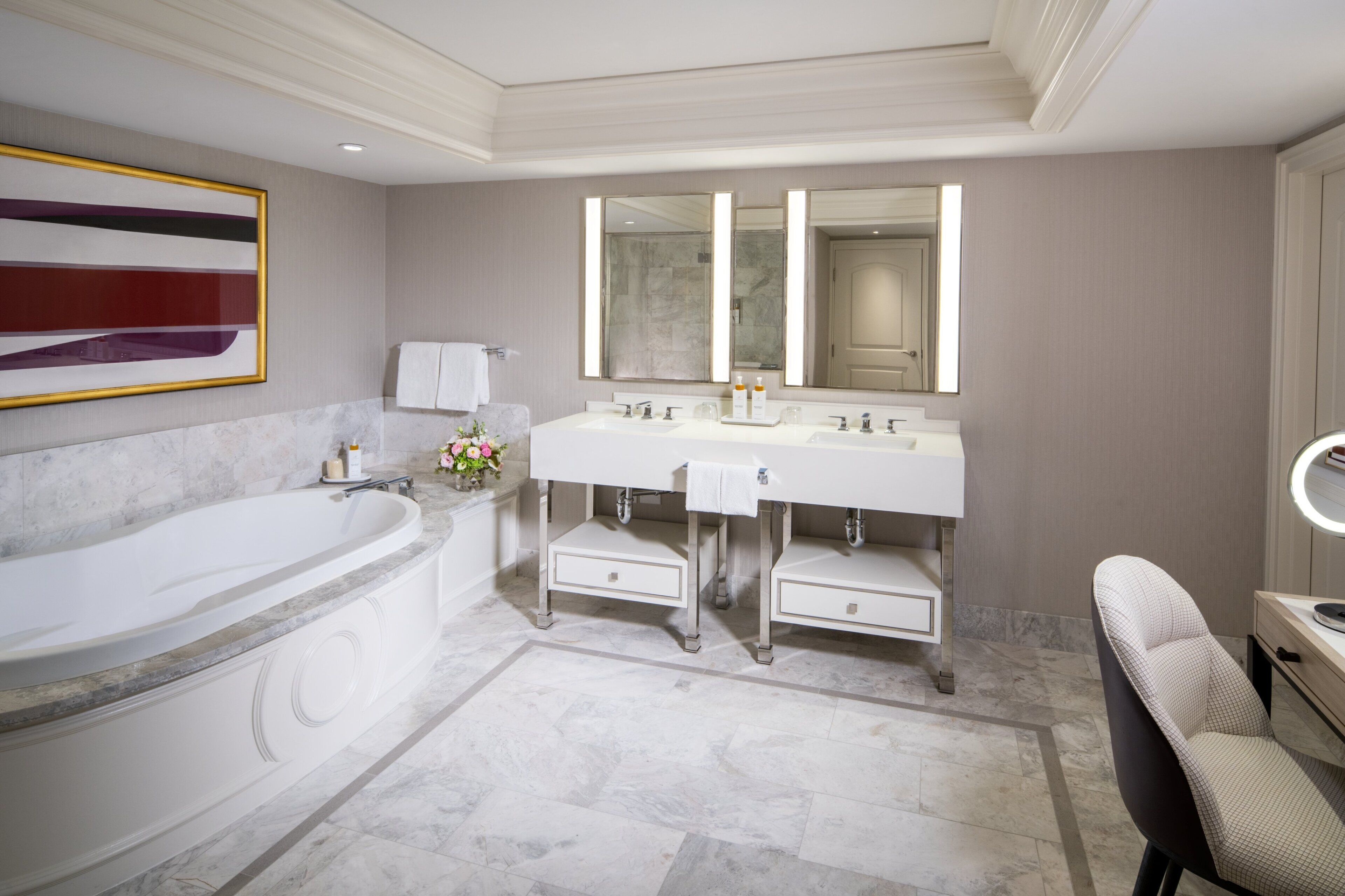 Een moderne badkamer met een groot bad, twee wastafels, een wastafelmeubel met een spiegel, en een stoel.