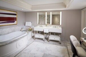 A modern bathroom with a large bathtub, two sinks, a vanity with a mirror, and a chair.