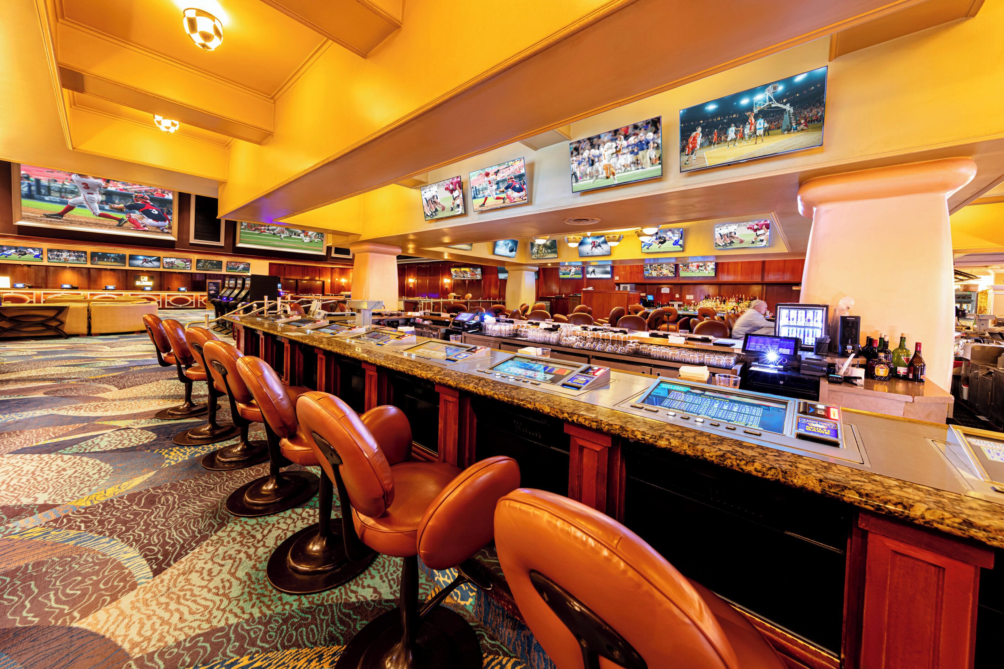 A bar area with multiple screens, bar stools, and a counter with various amenities.