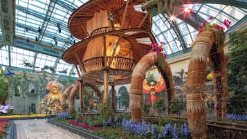 A grand atrium with a glass ceiling, ornate wooden structures, and lush floral arrangements.