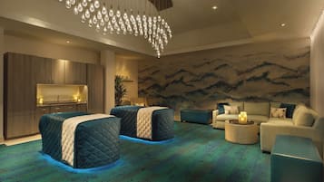 A modern hotel room with a large bed, a sofa, a coffee table, and a wall with a mountain mural.