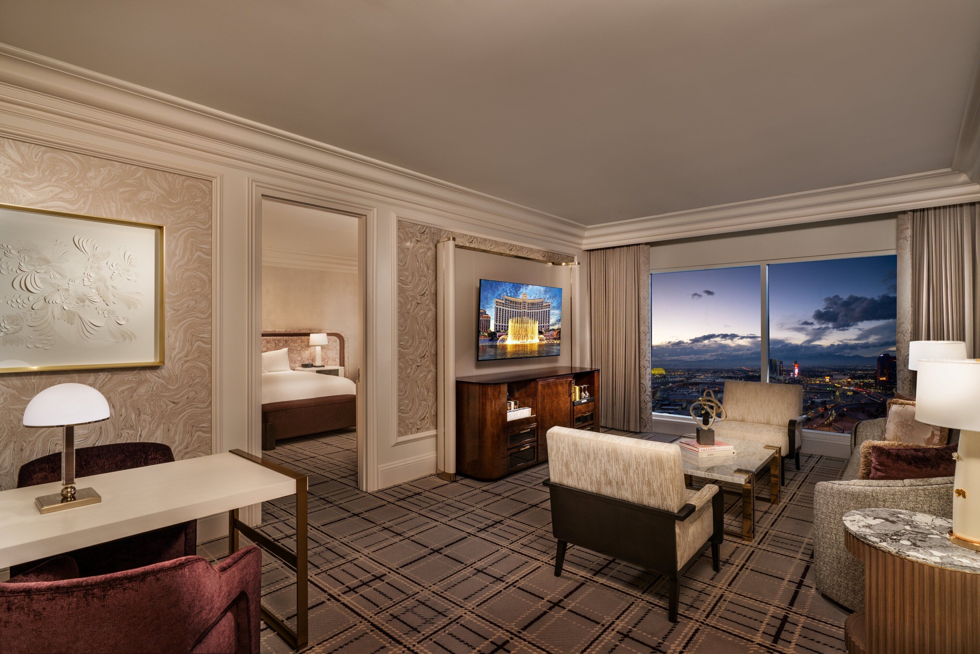 A hotel room with a large window, a television, a bed, a desk, and a chair.