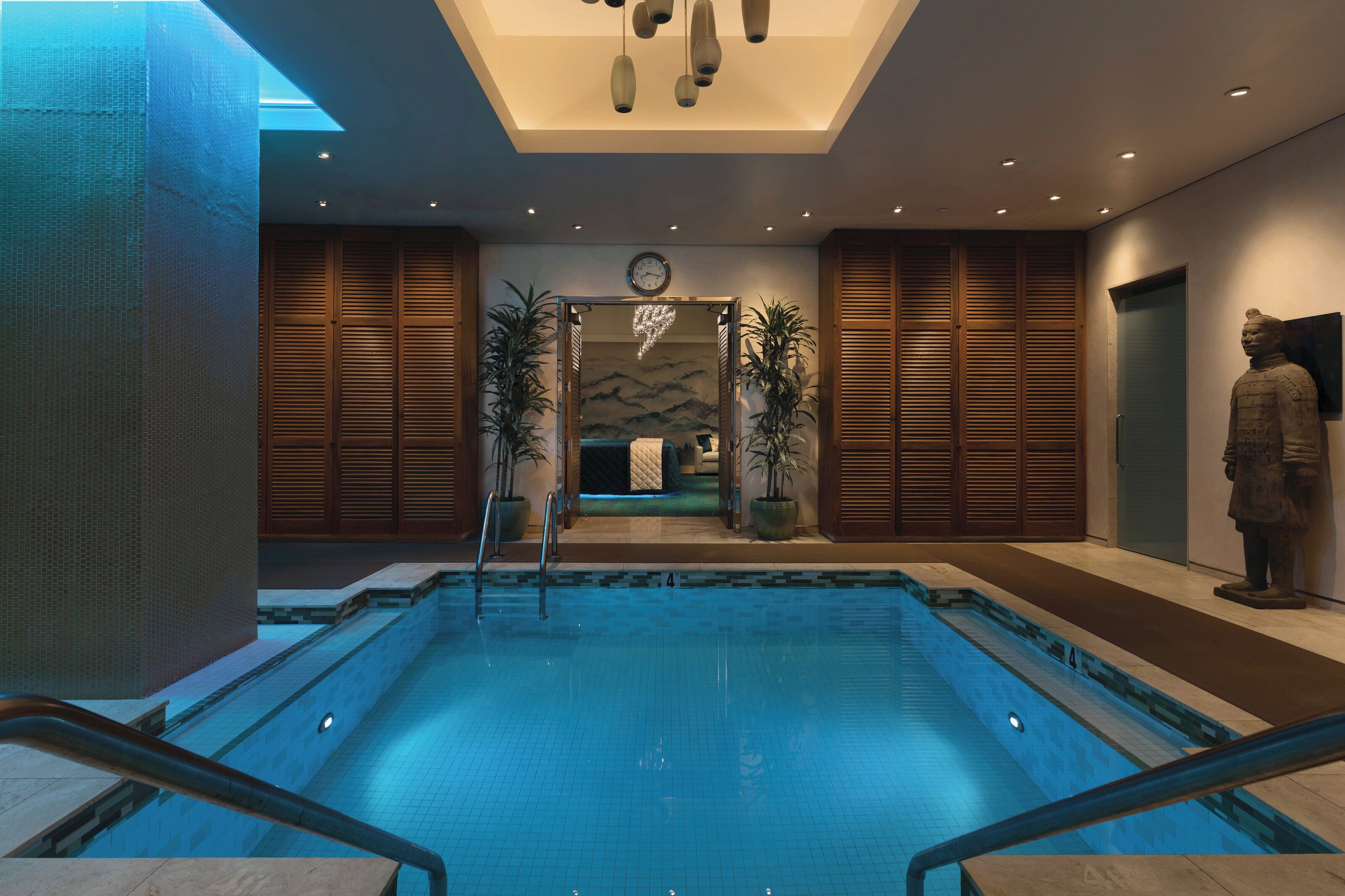 A swimming pool with a view of a mountain landscape through a glass wall, wooden doors, and a statue.