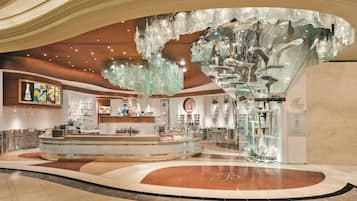 Een ruime lobby met een centraal receptiegedeelte, een grote kroonluchter en een bord met daarop 'Bellagio Patisserie'.